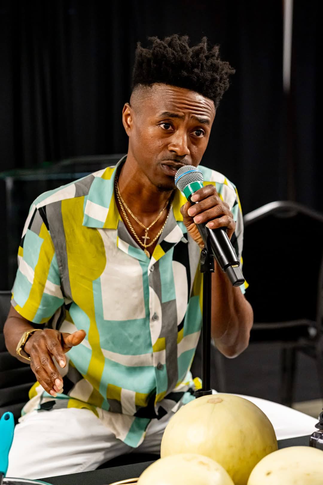 Marcus speaking on the mic with fresh melons on the demo table